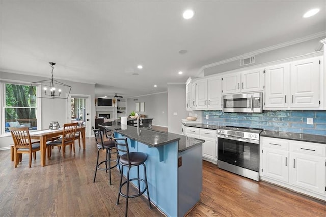 kitchen with crown molding, a center island, stainless steel appliances, white cabinetry, and visible vents