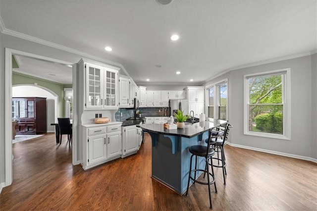 kitchen with ornamental molding, stainless steel fridge, plenty of natural light, white cabinetry, and arched walkways