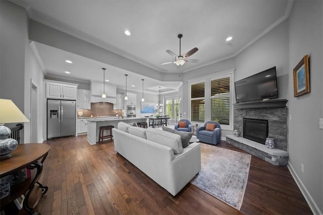 living area with a stone fireplace, ornamental molding, ceiling fan, and dark wood-style floors