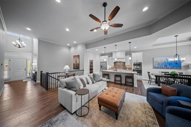 living room with ornamental molding, baseboards, recessed lighting, dark wood-type flooring, and ceiling fan with notable chandelier