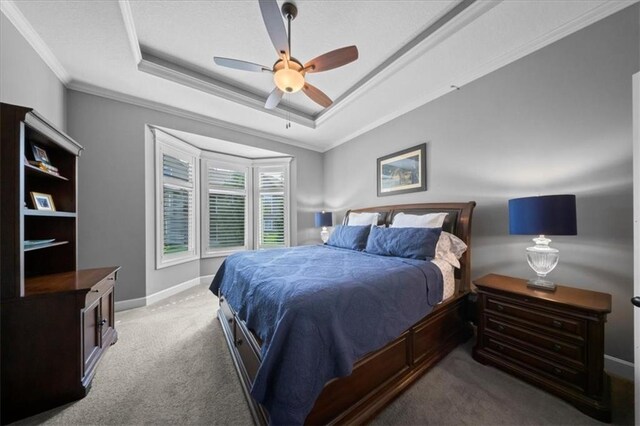 carpeted bedroom featuring baseboards, ornamental molding, ceiling fan, and a tray ceiling