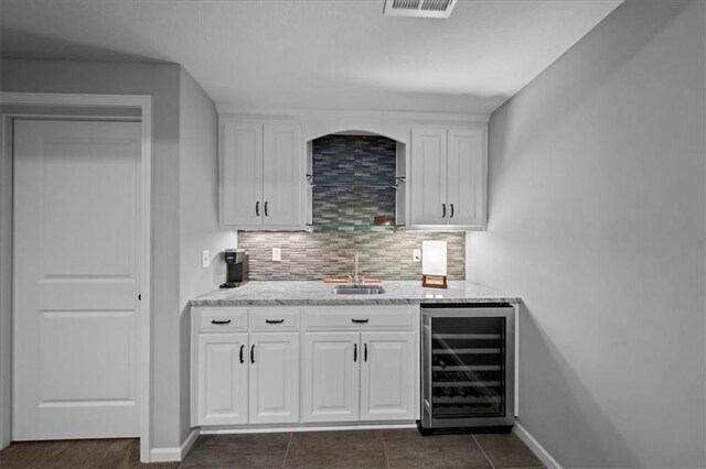 bar with decorative backsplash, visible vents, a sink, baseboards, and beverage cooler