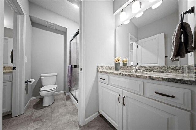bathroom with vanity, toilet, baseboards, a shower stall, and visible vents