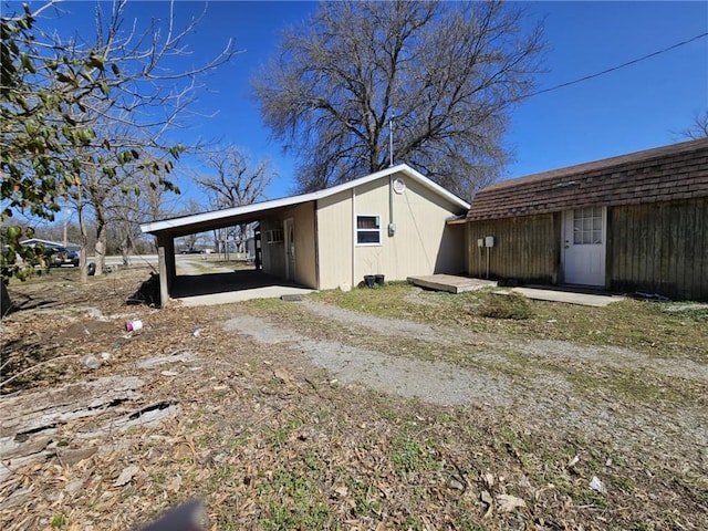 view of outbuilding with a carport, dirt driveway, and an outdoor structure
