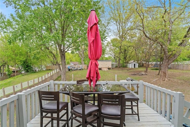 deck with a fenced backyard, a shed, a lawn, an outbuilding, and outdoor dining space