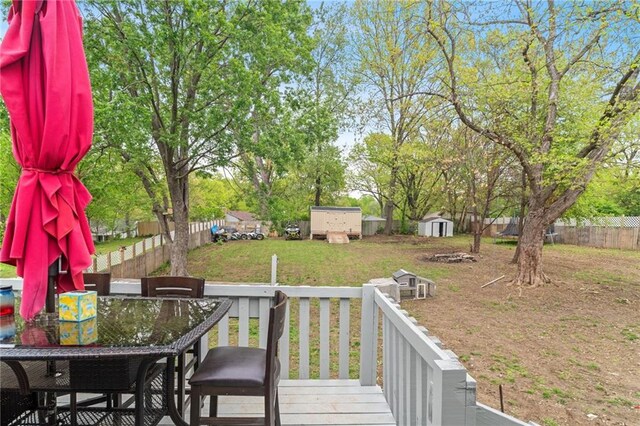 wooden deck featuring outdoor dining area, an outbuilding, a fenced backyard, a storage unit, and a yard