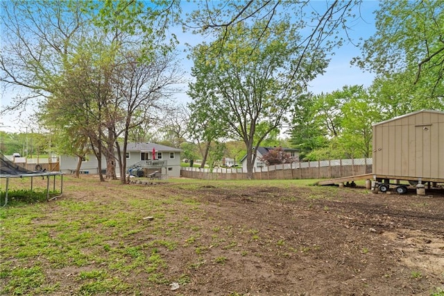 view of yard with fence, a storage unit, a trampoline, and an outdoor structure