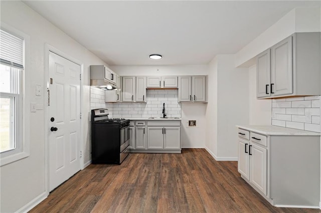 kitchen featuring dark wood-style flooring, a sink, gas stove, and tasteful backsplash