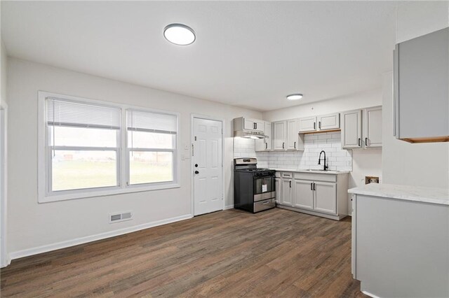 kitchen with decorative backsplash, visible vents, gas range, a sink, and dark wood-type flooring
