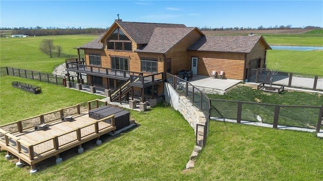 back of house featuring a deck with water view, fence, a shingled roof, and a lawn
