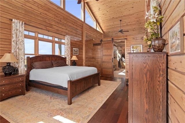 bedroom with wooden walls, a barn door, high vaulted ceiling, wood ceiling, and hardwood / wood-style flooring