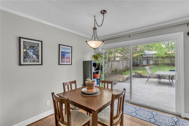 dining area with a textured ceiling, light wood finished floors, ornamental molding, and baseboards