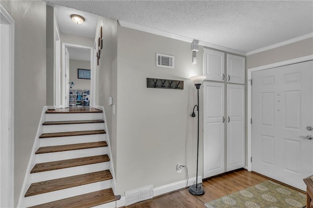entrance foyer featuring a textured ceiling, stairway, visible vents, light wood-type flooring, and ornamental molding