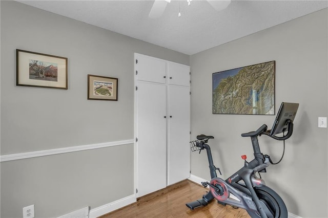 exercise room with baseboards, wood finished floors, a ceiling fan, and a textured ceiling