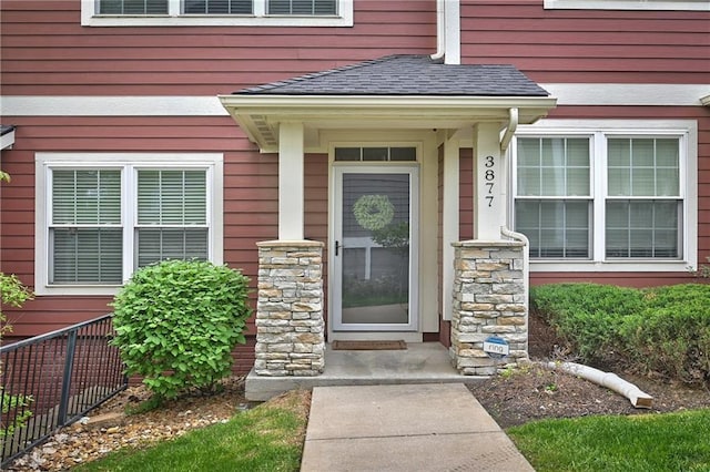 entrance to property featuring roof with shingles and stone siding