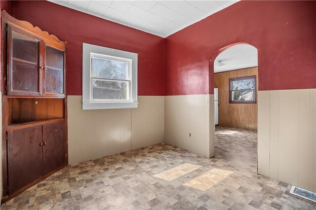 707 E 8th St, Trenton, MO 64683 - empty room featuring wood walls, a wainscoted wall, visible vents, and arched walkways
