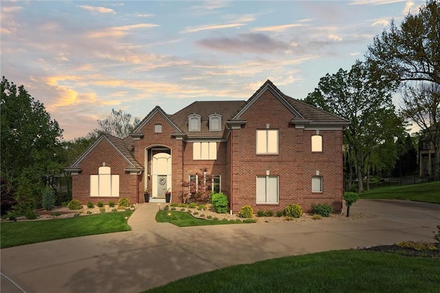 traditional-style home featuring curved driveway, a front yard, and brick siding