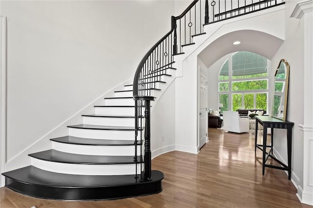staircase featuring baseboards, wood finished floors, and a towering ceiling