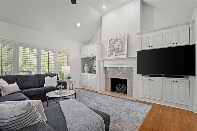 living area with light wood-type flooring, recessed lighting, a fireplace, and high vaulted ceiling