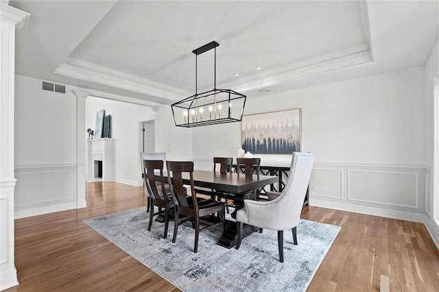 dining room with visible vents, ornate columns, wood finished floors, and a tray ceiling