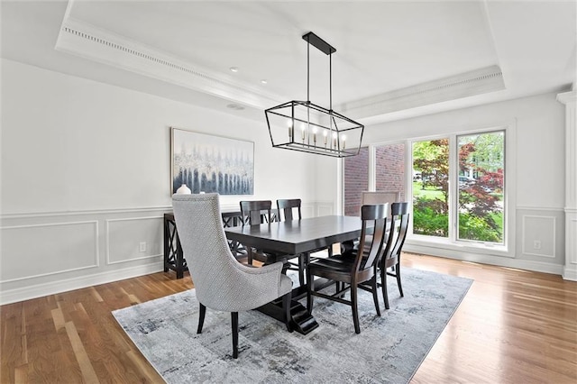 dining area featuring a decorative wall, a tray ceiling, wood finished floors, and a chandelier