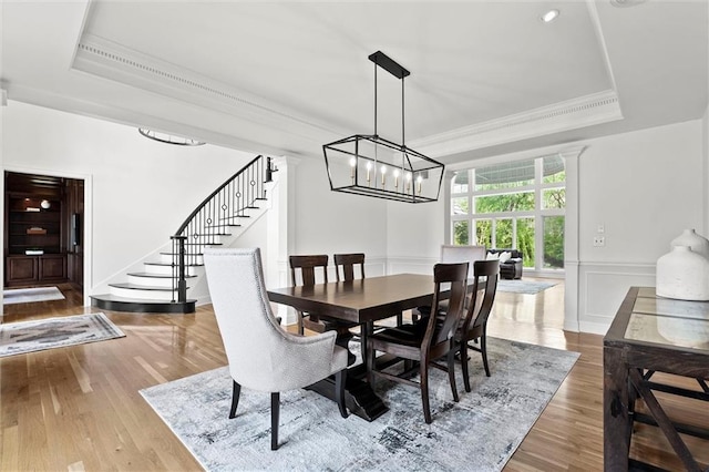 dining space with crown molding, stairway, wood finished floors, and a raised ceiling