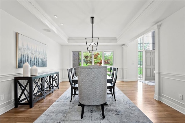 dining space featuring a tray ceiling, a decorative wall, wood finished floors, and a healthy amount of sunlight