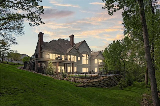 rear view of property featuring a lawn, stucco siding, fence, and a balcony