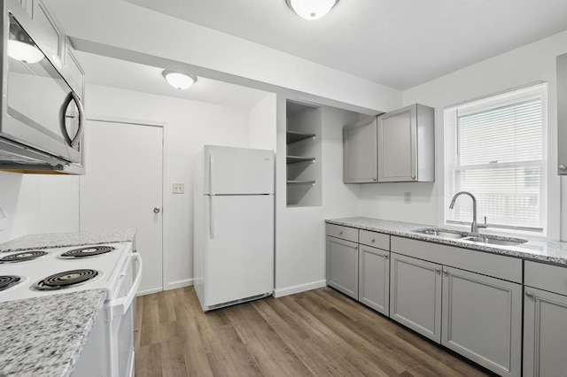 kitchen featuring white appliances, gray cabinetry, a sink, and wood finished floors