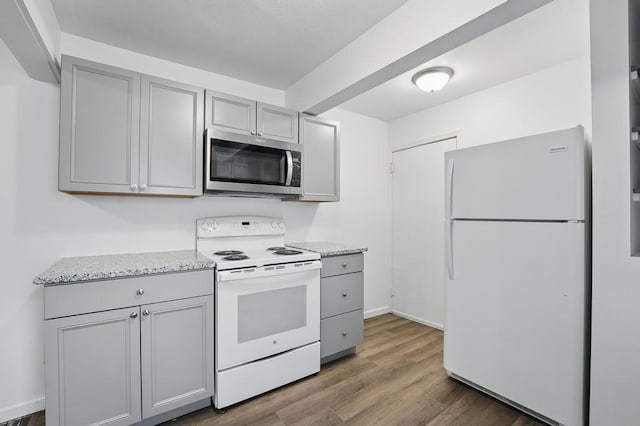 kitchen with white appliances, gray cabinets, wood finished floors, and light stone counters