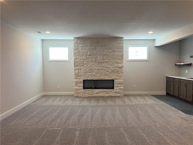 24919 W 145th St, Olathe, KS 66061 - unfurnished living room featuring healthy amount of natural light, carpet floors, a textured ceiling, a stone fireplace, and baseboards