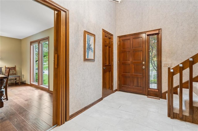 foyer featuring stairway, baseboards, and wallpapered walls