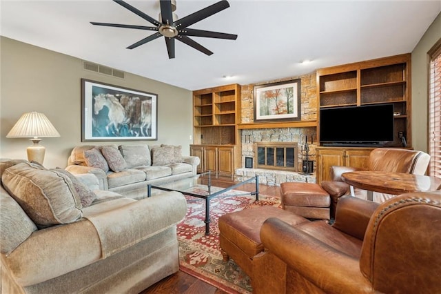 living room with visible vents, built in features, wood finished floors, a stone fireplace, and ceiling fan