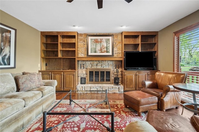 living area with a stone fireplace, built in features, ceiling fan, and wood finished floors