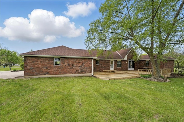 rear view of house featuring a lawn, a wooden deck, brick siding, a patio, and a shingled roof