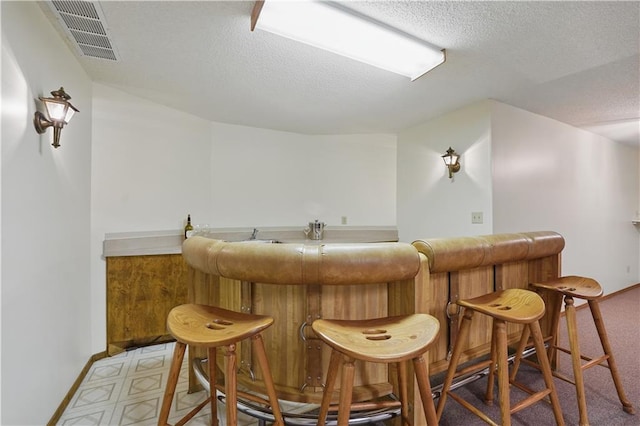 bar with a textured ceiling, visible vents, a dry bar, and baseboards