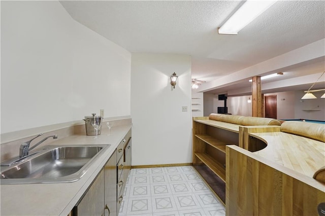 kitchen featuring open shelves, baseboards, light floors, light countertops, and a sink