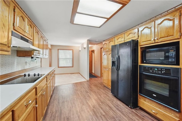 kitchen featuring light wood-style floors, light countertops, baseboards, under cabinet range hood, and black appliances