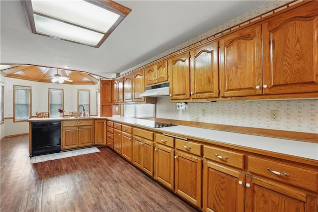 kitchen featuring brown cabinetry, a peninsula, under cabinet range hood, and black appliances