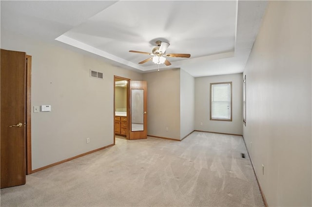 unfurnished room with a ceiling fan, light colored carpet, visible vents, a raised ceiling, and baseboards