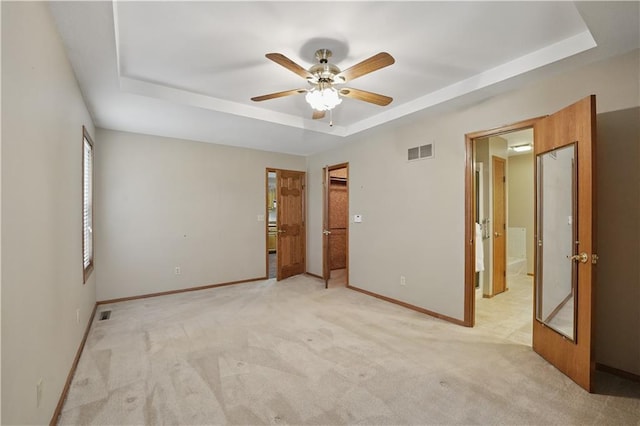 unfurnished bedroom with baseboards, a tray ceiling, light colored carpet, and visible vents