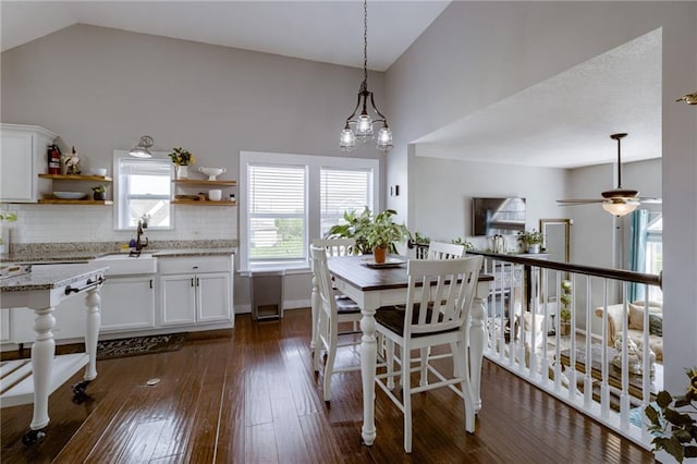 dining space with a ceiling fan, dark wood-style flooring, high vaulted ceiling, and baseboards