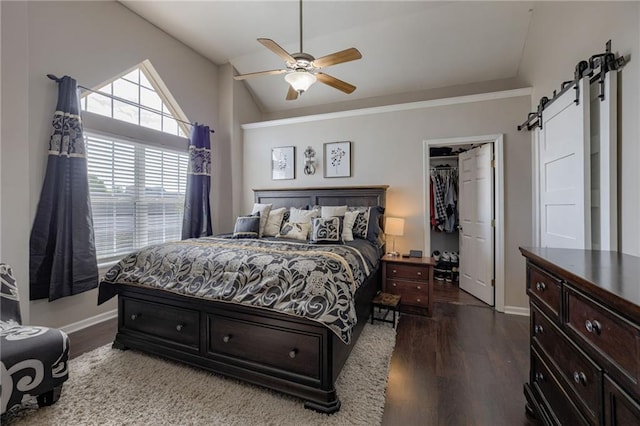 bedroom featuring a barn door, dark wood finished floors, baseboards, vaulted ceiling, and a walk in closet