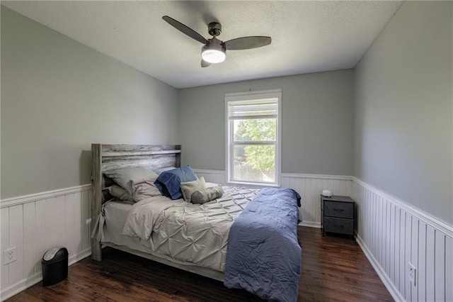bedroom featuring wainscoting, wood finished floors, ceiling fan, and a textured ceiling