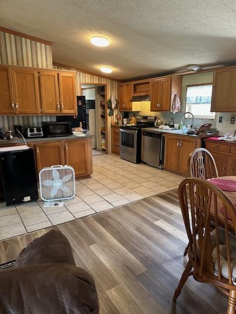 4323 NW County Road 17402nd St, Adrian, MO 64720 - kitchen with appliances with stainless steel finishes, under cabinet range hood, a textured ceiling, brown cabinetry, and light tile patterned floors