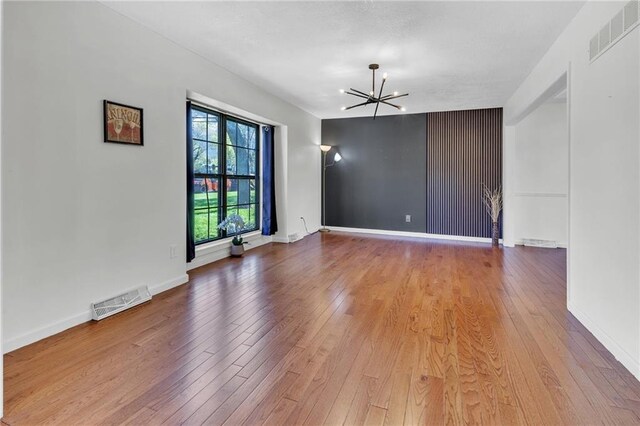 spare room with visible vents, hardwood / wood-style floors, and a chandelier