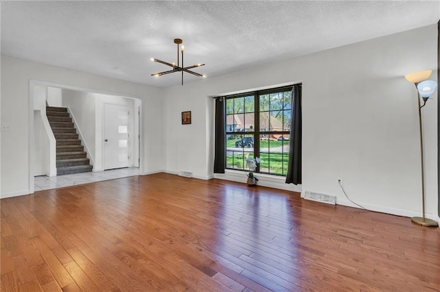 unfurnished living room featuring stairway, wood-type flooring, a notable chandelier, visible vents, and a textured ceiling