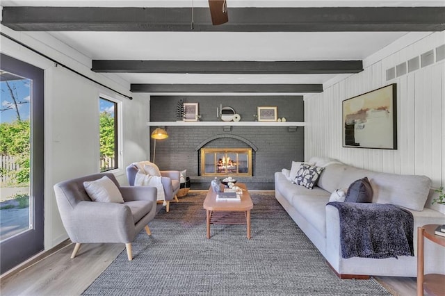 living area with wood finished floors, baseboards, beamed ceiling, and a brick fireplace