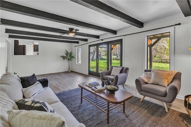 living area with wood finished floors, plenty of natural light, beamed ceiling, and baseboards