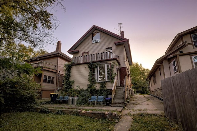rear view of house featuring stairs, a balcony, and fence